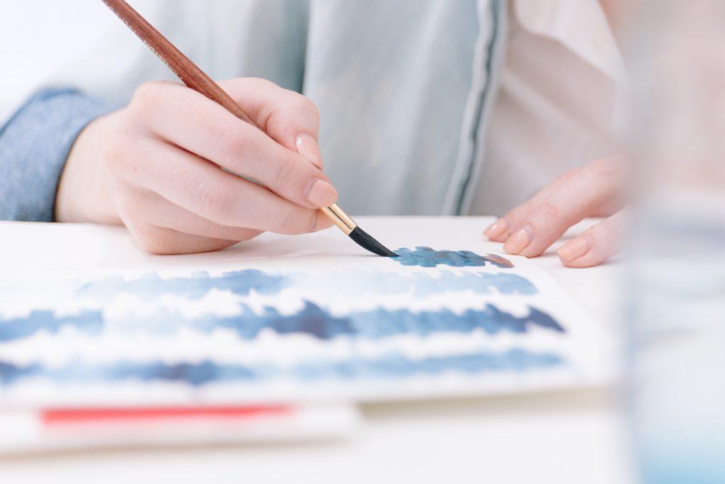 person painting blue lines on a white piece of paper