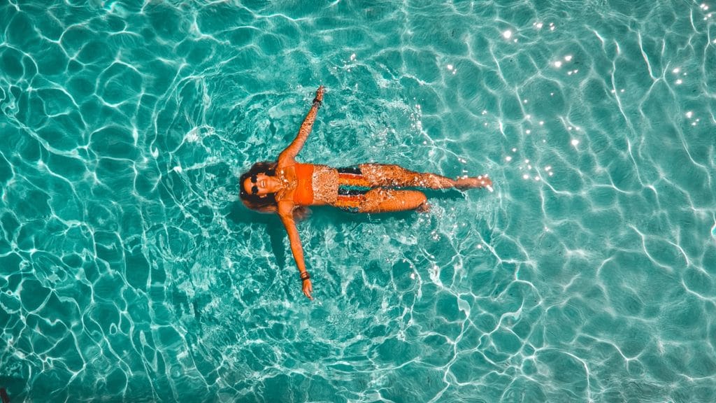 a birds eye view of a woman floating in an orange bikini in a turquoise pool