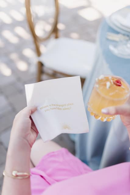 White woman holding conversation starter napkin Convokins with cocktail in right hand