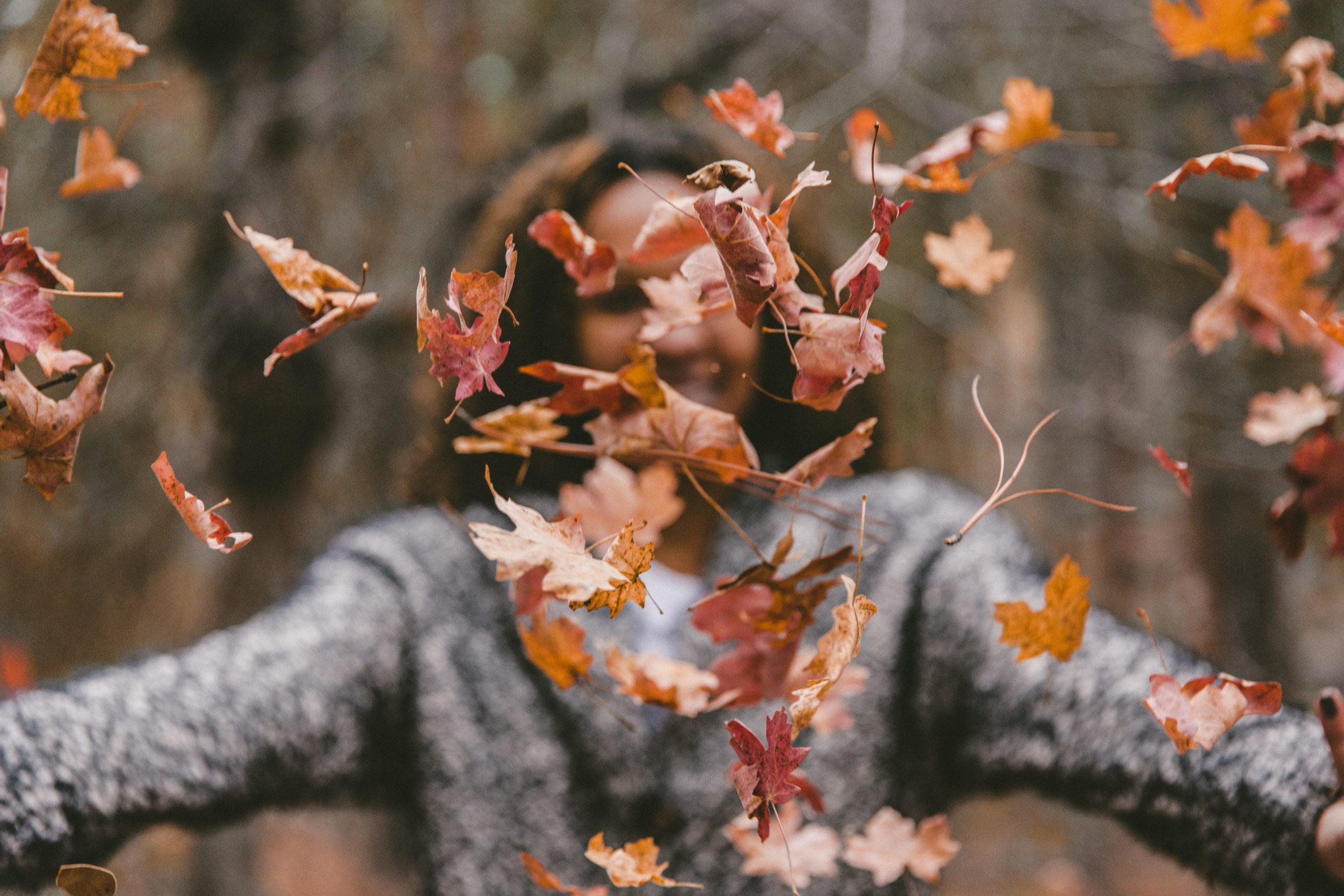woman throwing up fall leaves out of focus