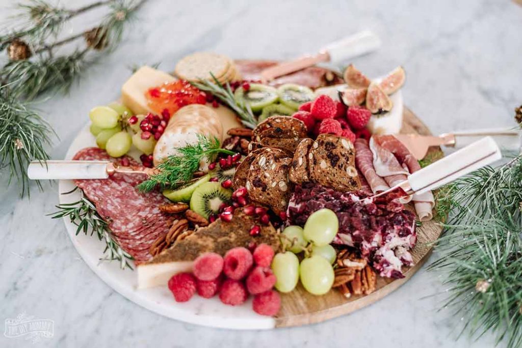 a meat filled cheeseboard with serving spoons on a marble table