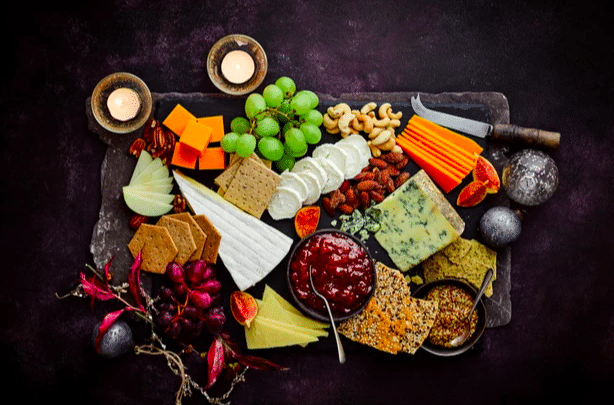 a flat lay of christmas cheeseboards filled with food, a knife and candles