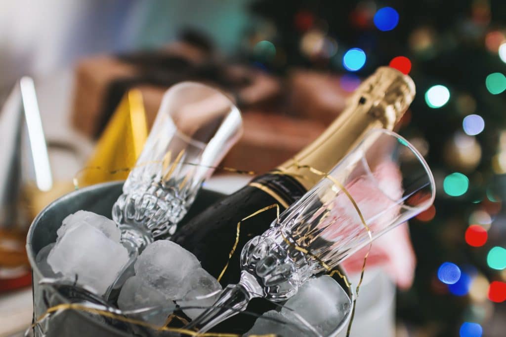 an ice bucket filled with ice and champagne and glasses with some gold christmas holiday decorating around it