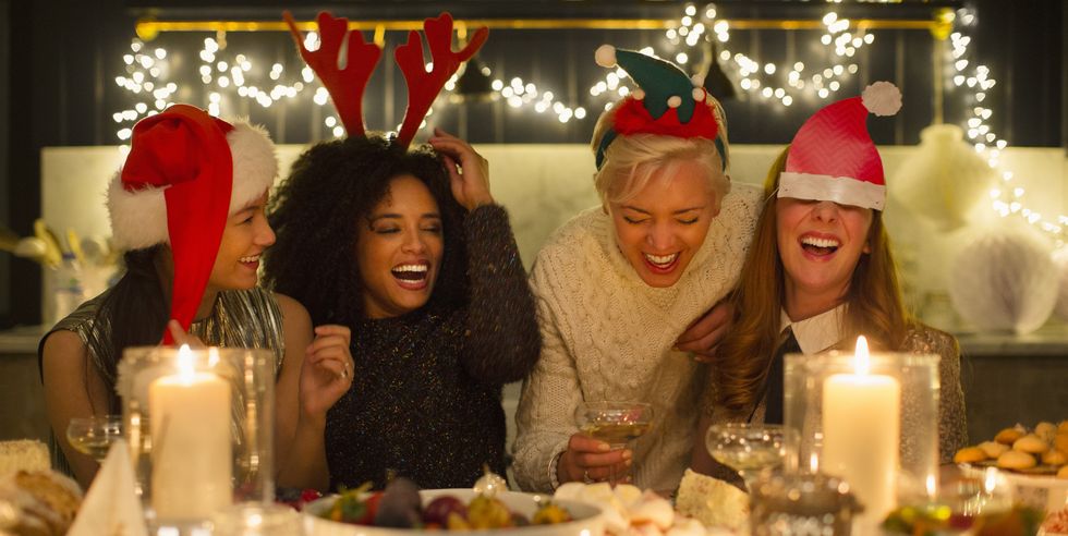 a group of friends wearing christmas hats and laughing surrounded by candles and lights