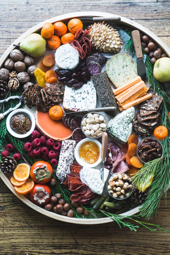 a flat lay of a round christmas cheeseboard with nuts, meat, cheese and pine