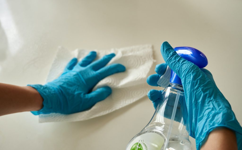 a pair of hands holding cleaning spray and wiping a surface