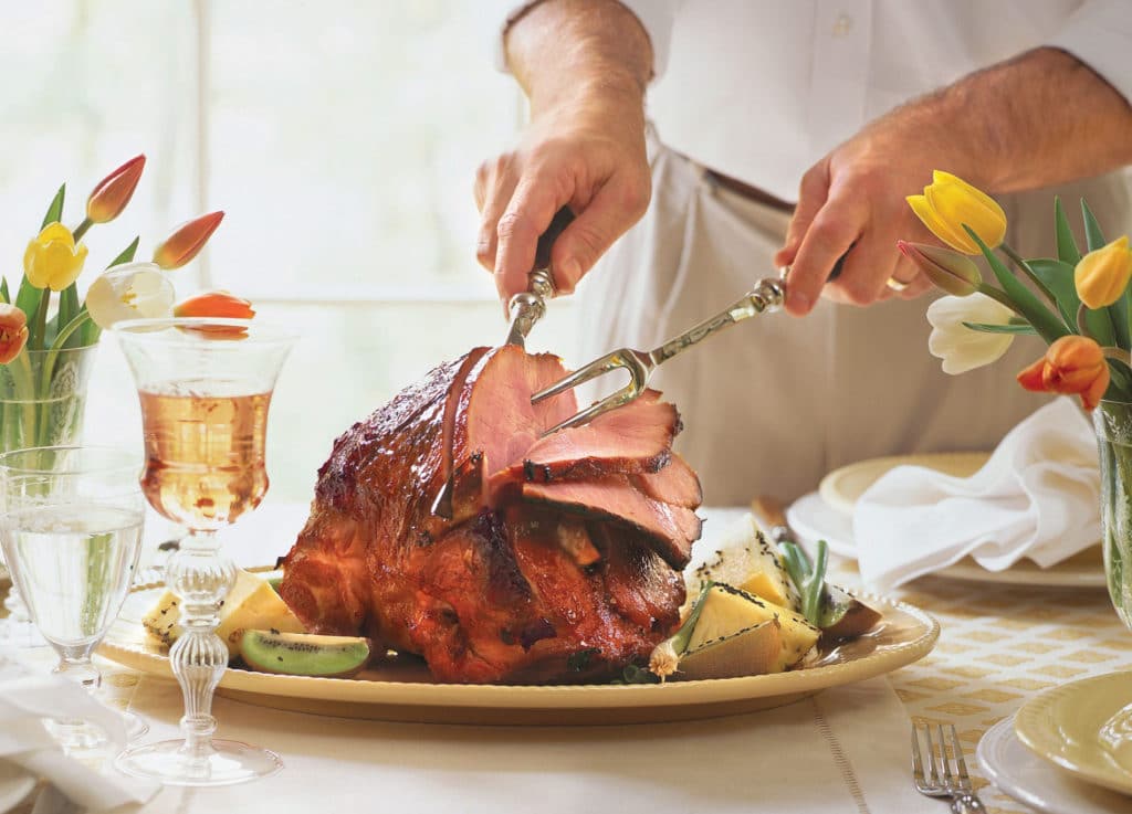 man cutting glazed ham on an easter table setting