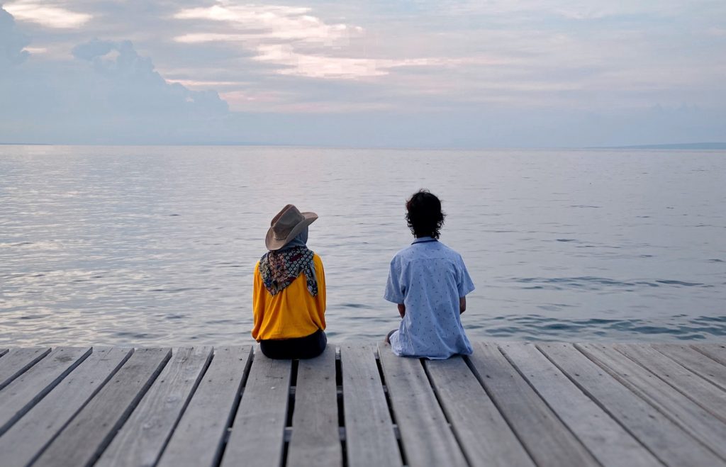 two people sat on a bridge looking out to water deep conversation starters