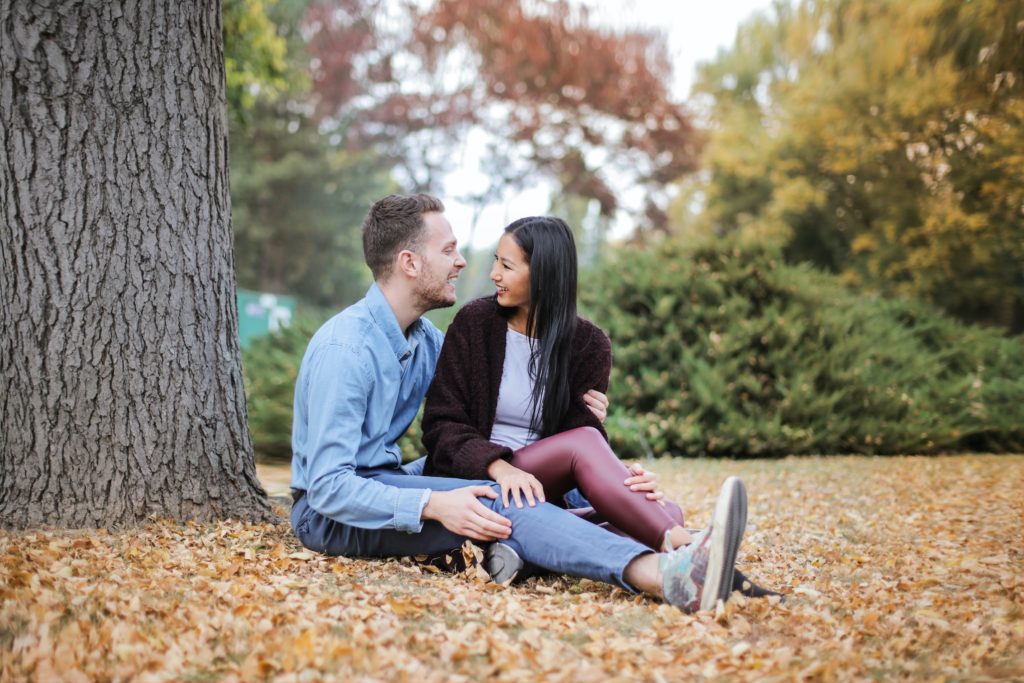 a couple smiling at each other sitting down in a park deep conversation starters