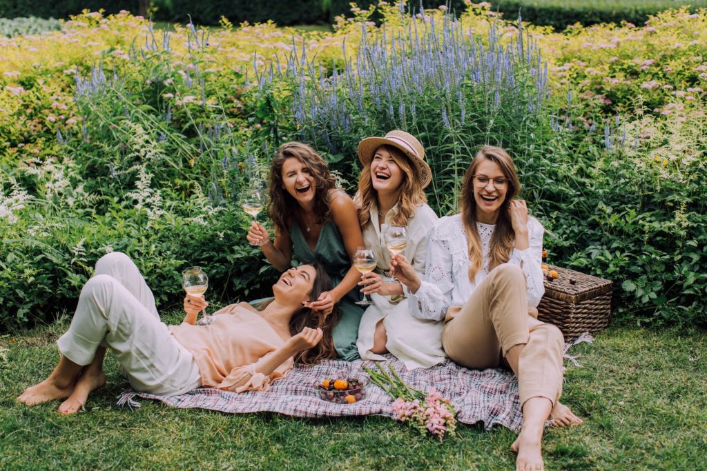 a group of women drinking wine at a picnic laughing together